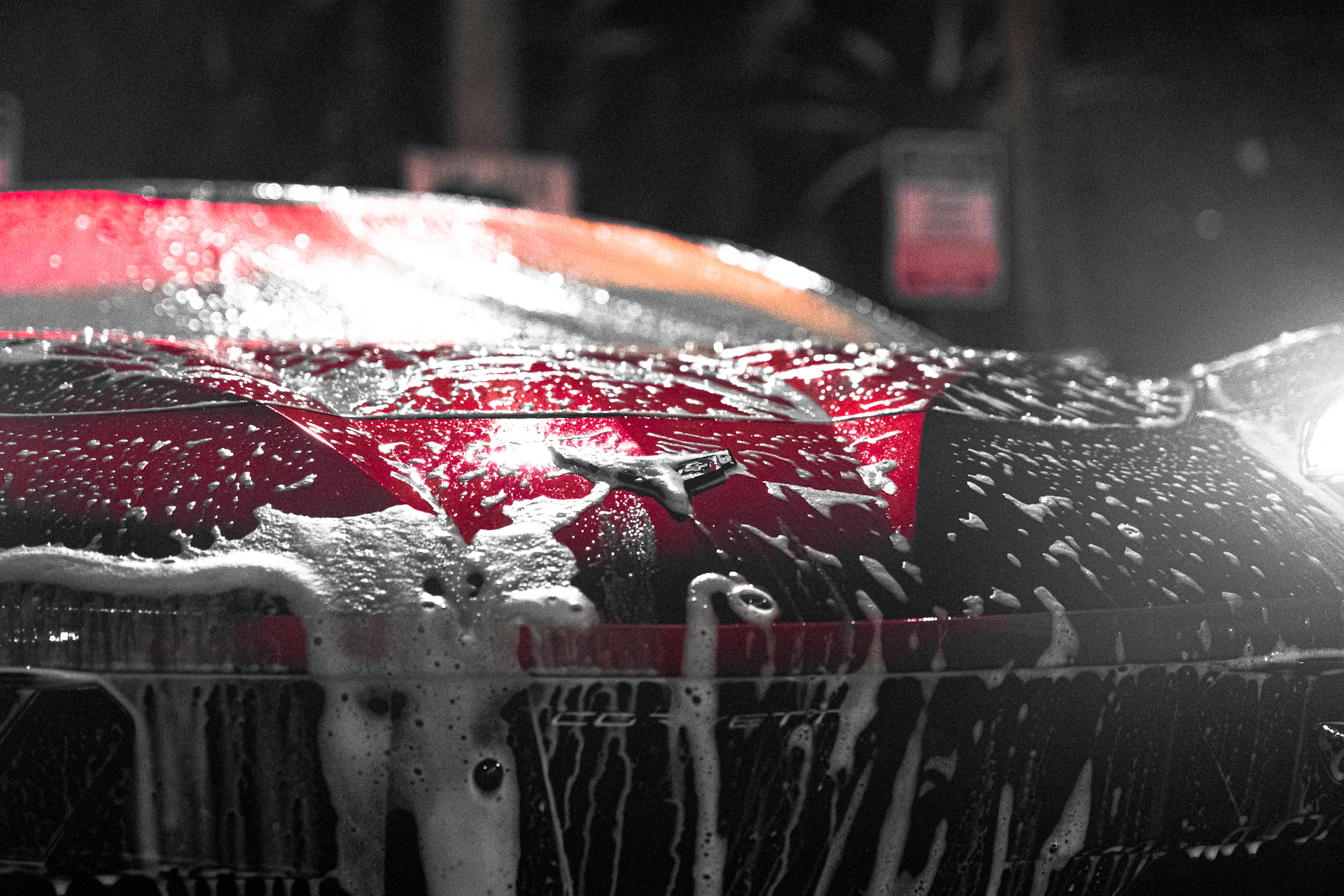 Red Chevrolet Corvette C8 blanketed in thick foam cannon suds during a hand wash