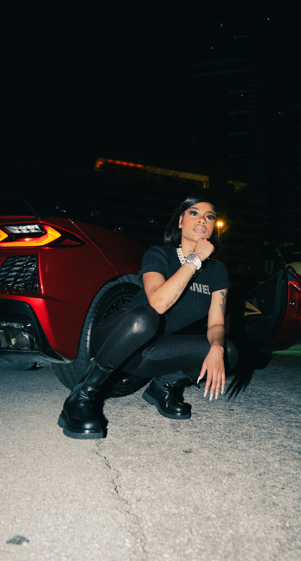 a woman sitting on the ground next to a red sports car