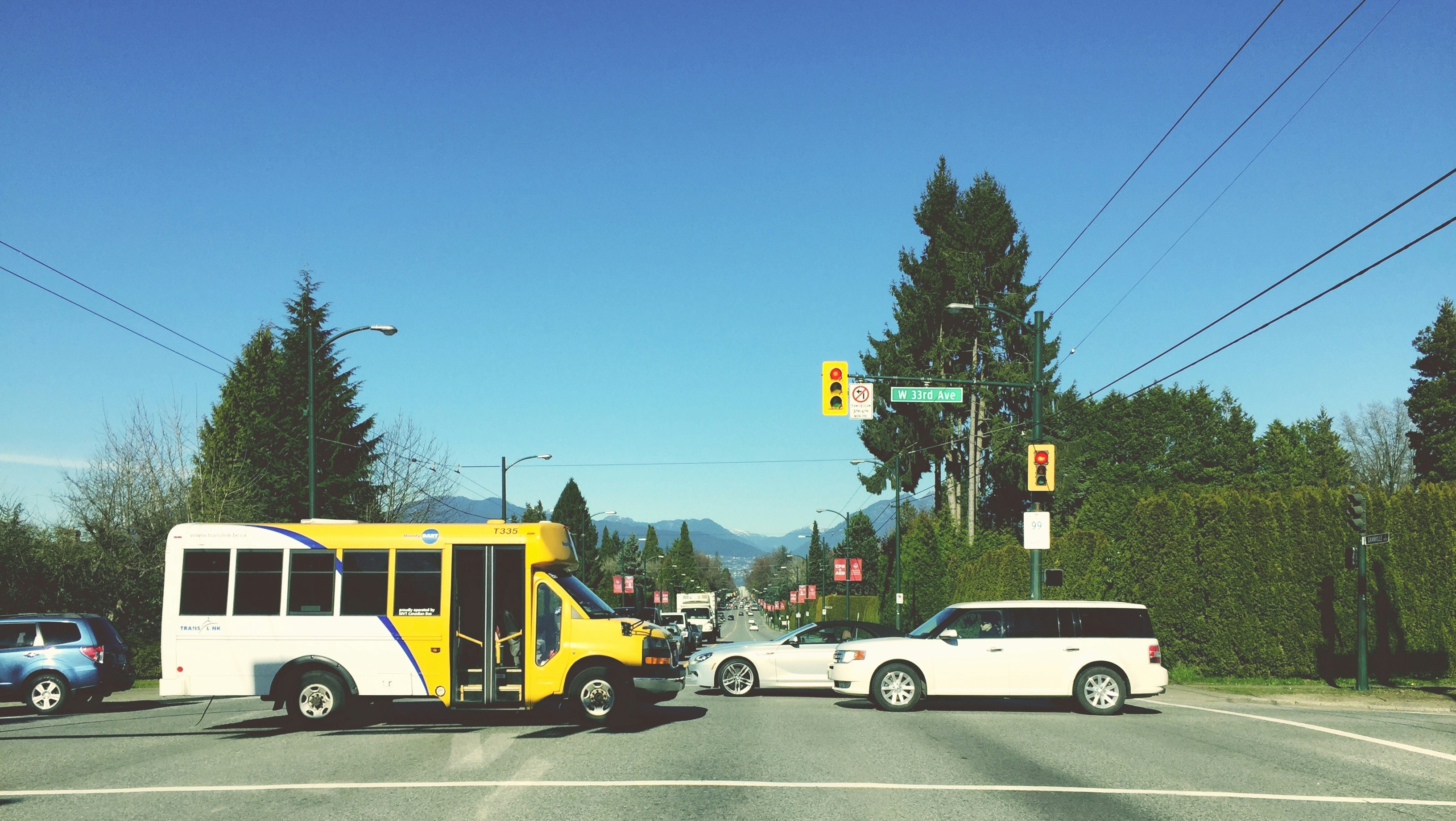 a yellow and white bus driving down a street next to a white car