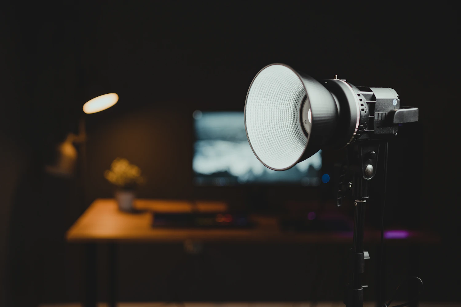A lighting head and a monitor burning in a dark room, the rest of the bench in shadow