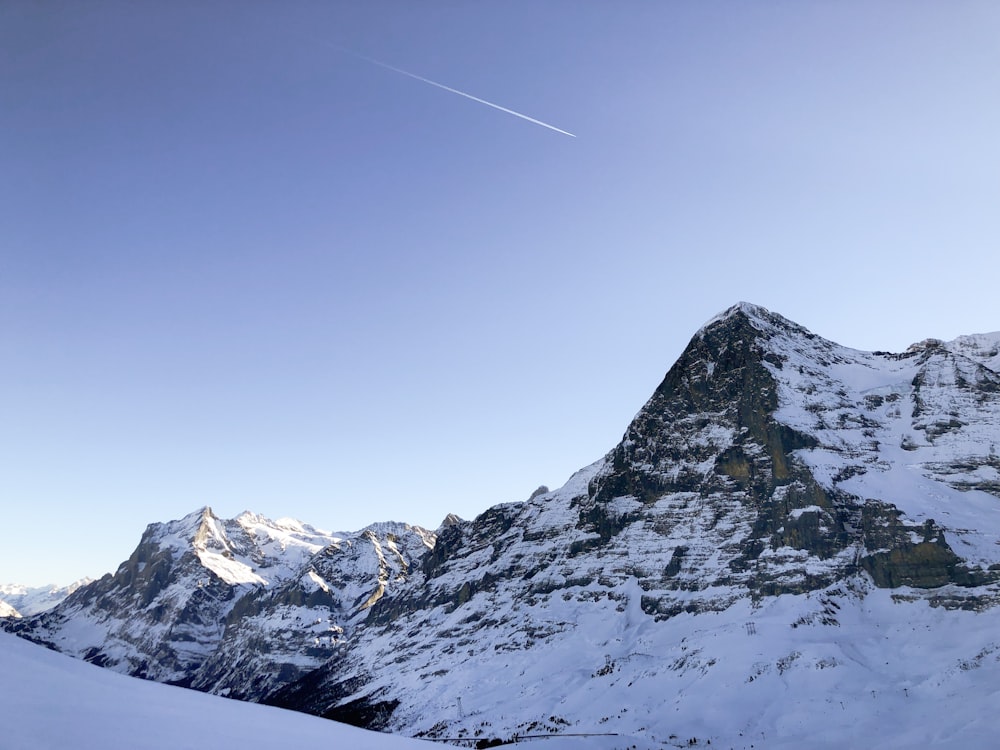 a snow covered mountain with a plane flying in the sky