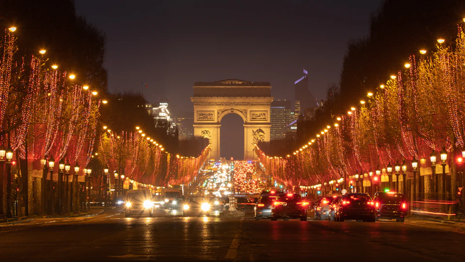 The Champs-Élysées at night, its trees wrapped in red Christmas lights and the Arc de Triomphe at the end of the avenue