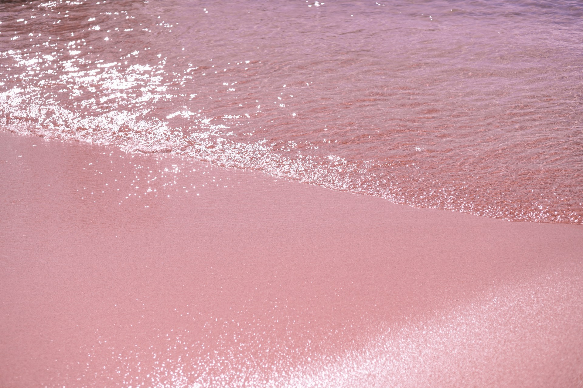 a pink beach with a wave coming in to shore