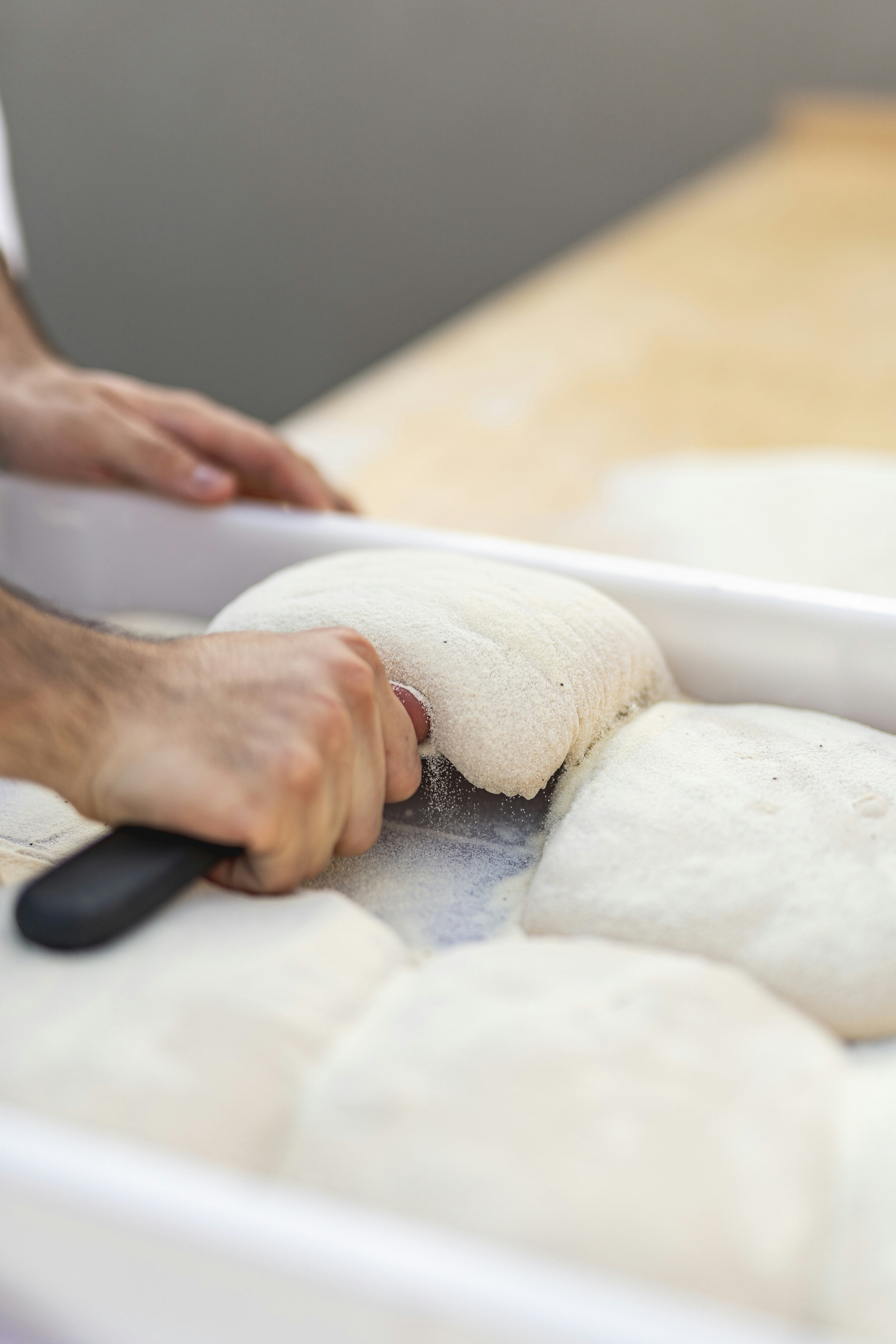 Hands using a bench scraper to cut and fold bread dough portions