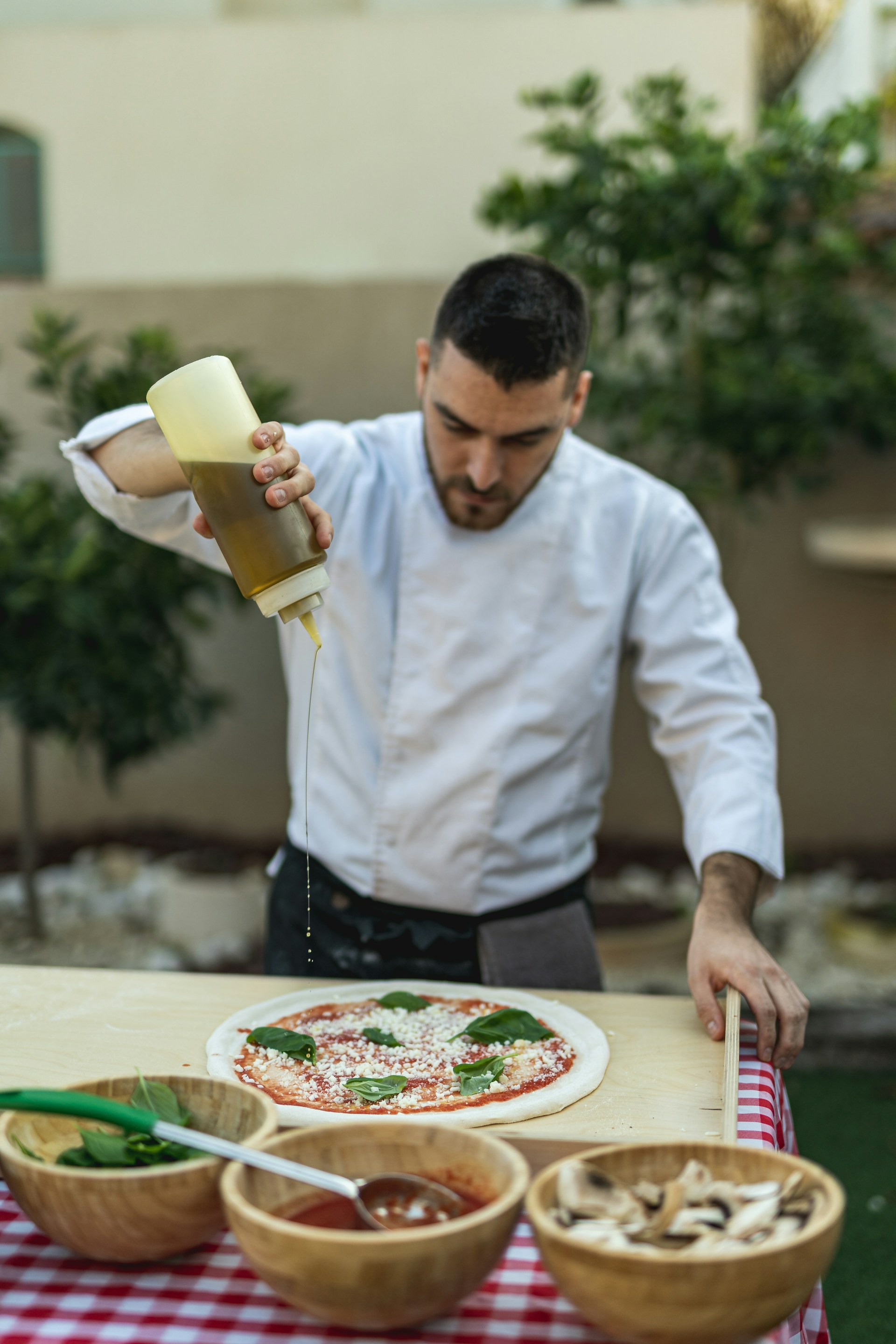 a man pouring sauce on a pizza on a table