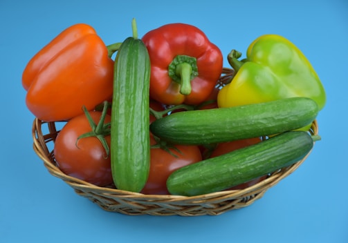 A basket filled with a variety of fresh colorful fruits and vegetables on a wooden table.