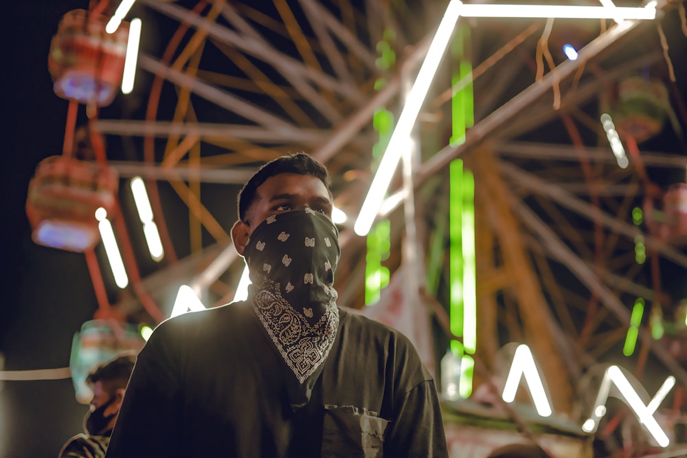 a man wearing a bandana standing in front of a ferris wheel