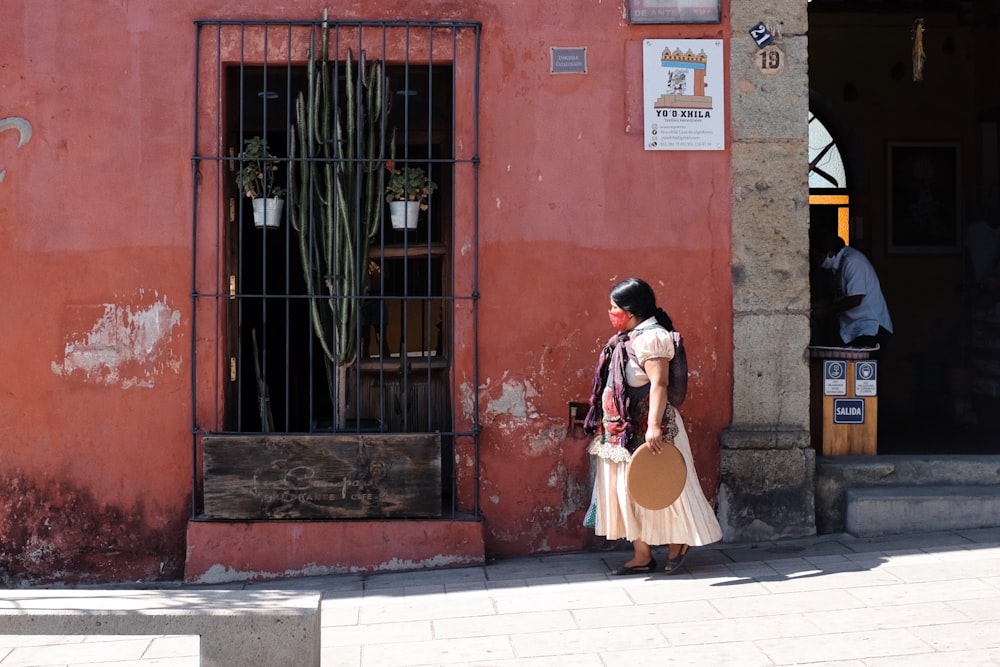 a woman walking down a street past a red building