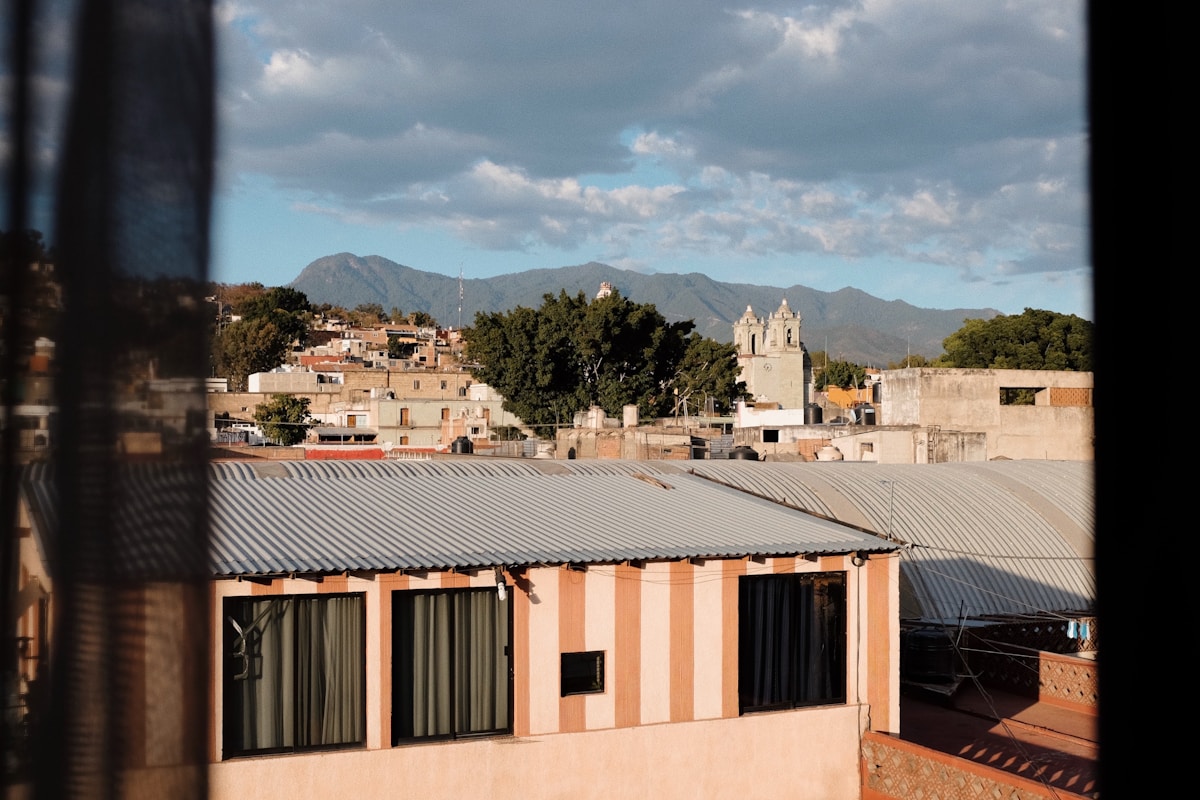 Rooftop view of Oaxaca de Juárez, Mexico, with colonial buildings, church towers, and the Sierra Madre mountains rising in the distance