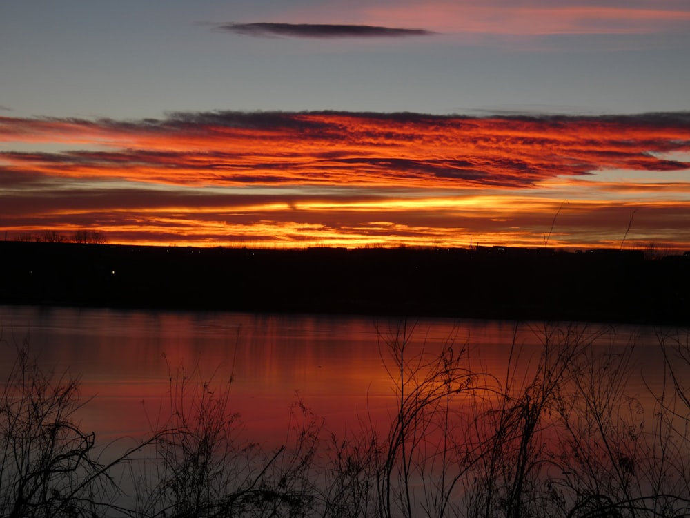 the sun is setting over a lake with tall grass