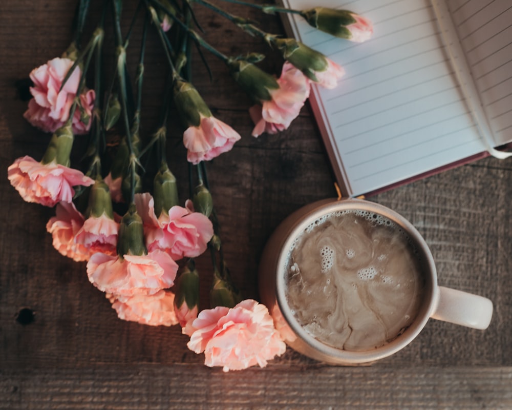 a cup of coffee next to a book and flowers