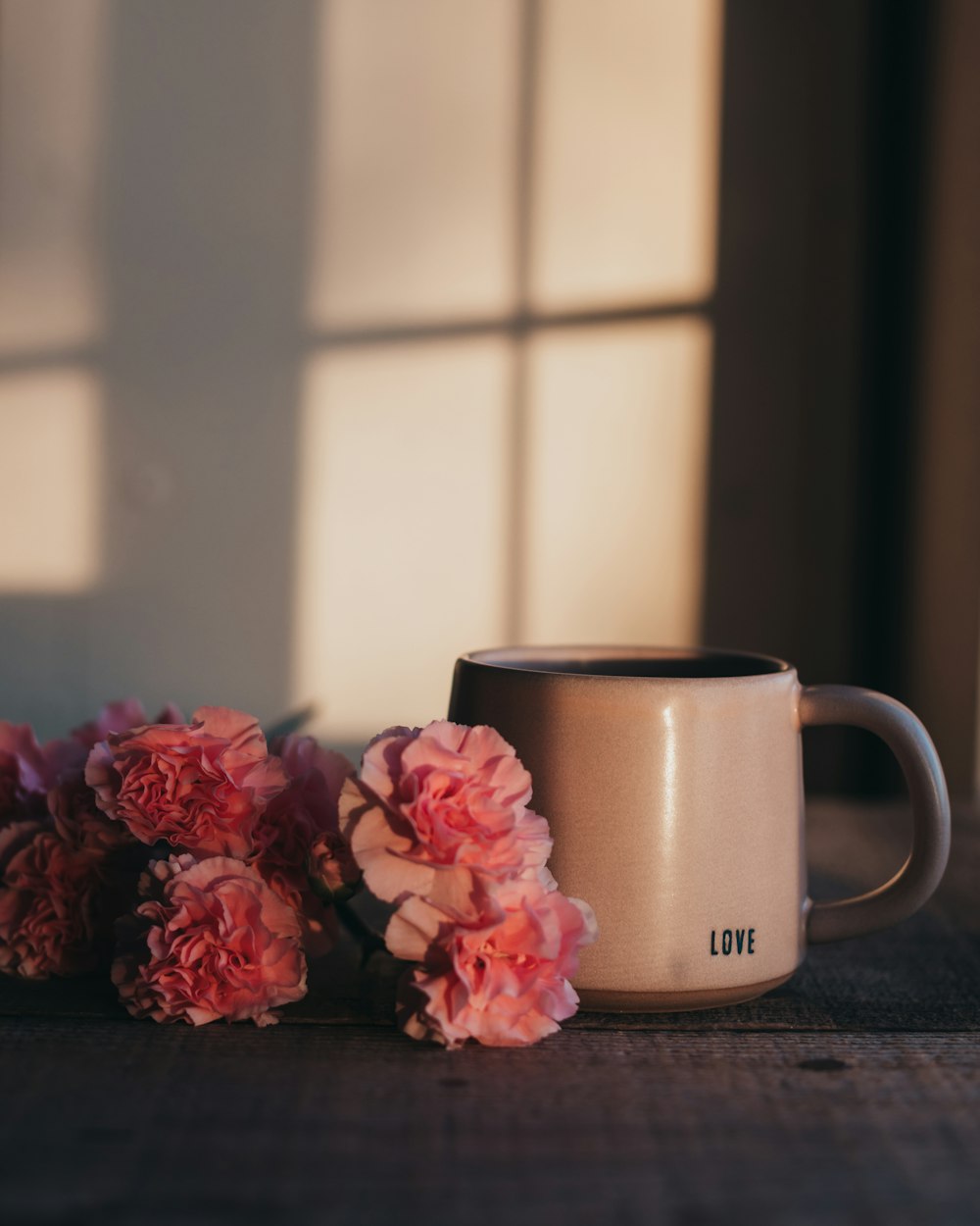 a coffee cup sitting on top of a table next to pink flowers