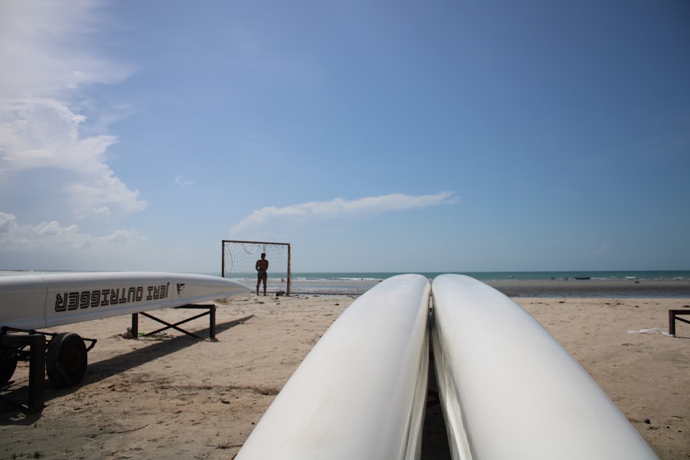 Un hombre parado junto a una tabla de surf blanca en una playa