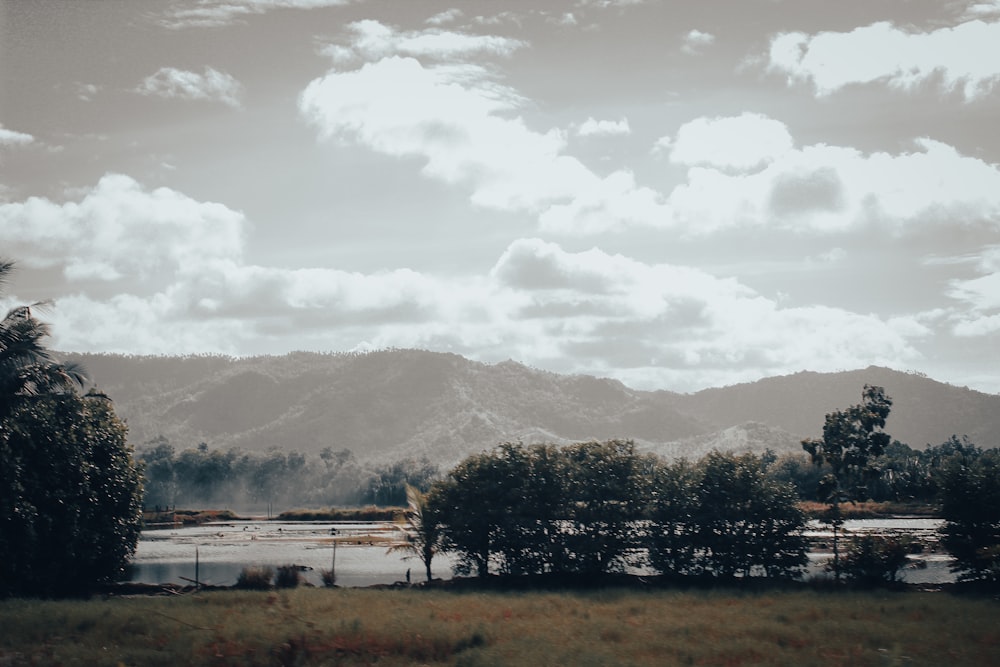 a lake surrounded by trees and mountains under a cloudy sky