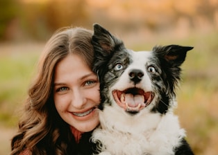 A warm photo of Brianna and Luca smiling with a happy dog in a sunlit park.