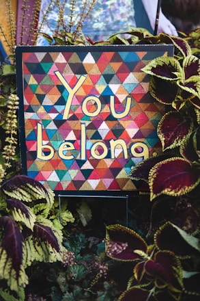 a sign that says you belong surrounded by plants