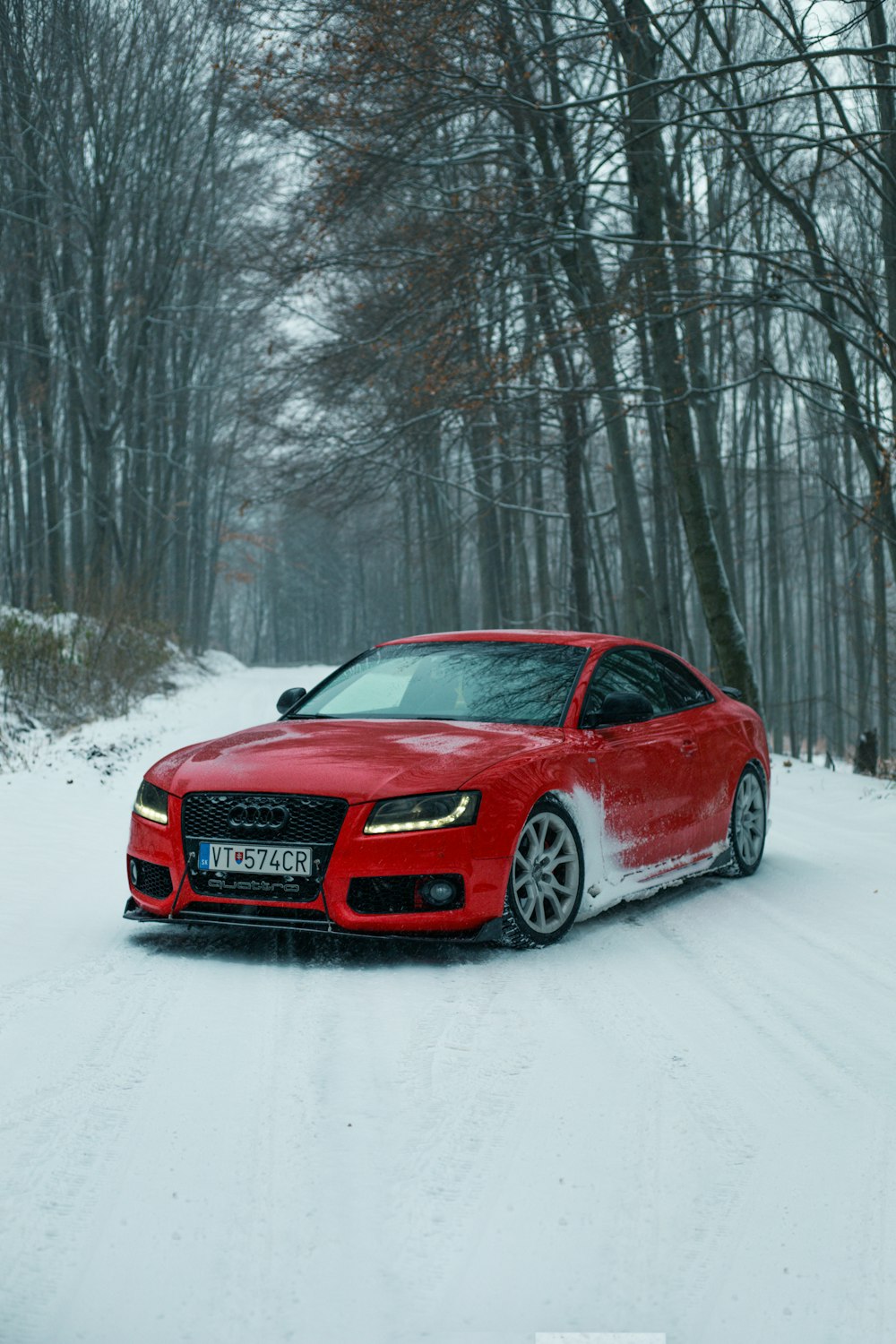 a red car driving down a snow covered road