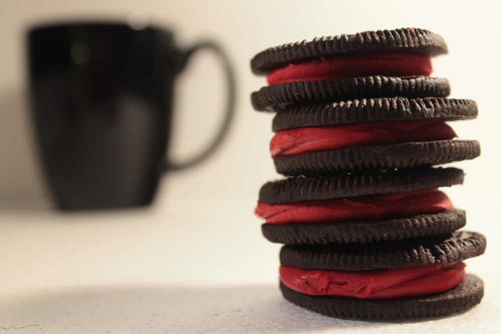 a stack of red and black cookies next to a cup of coffee