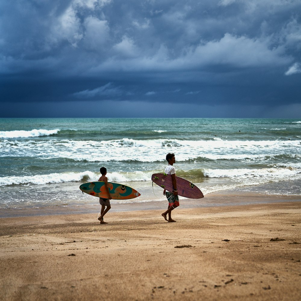 une personne portant une planche de surf au sommet d’une plage de sable
