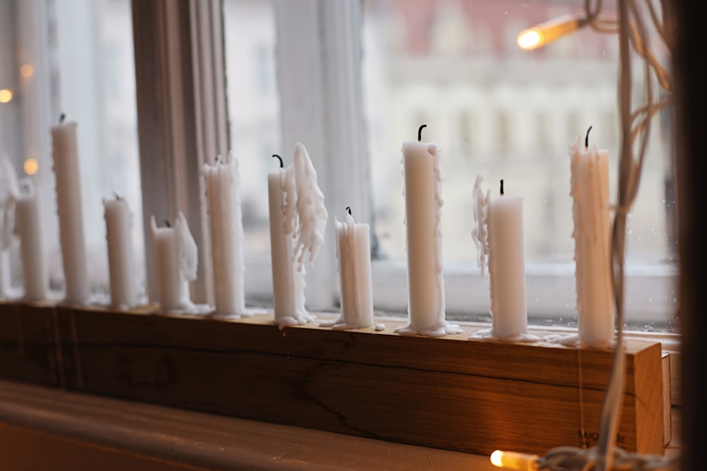 a row of white candles sitting on top of a window sill