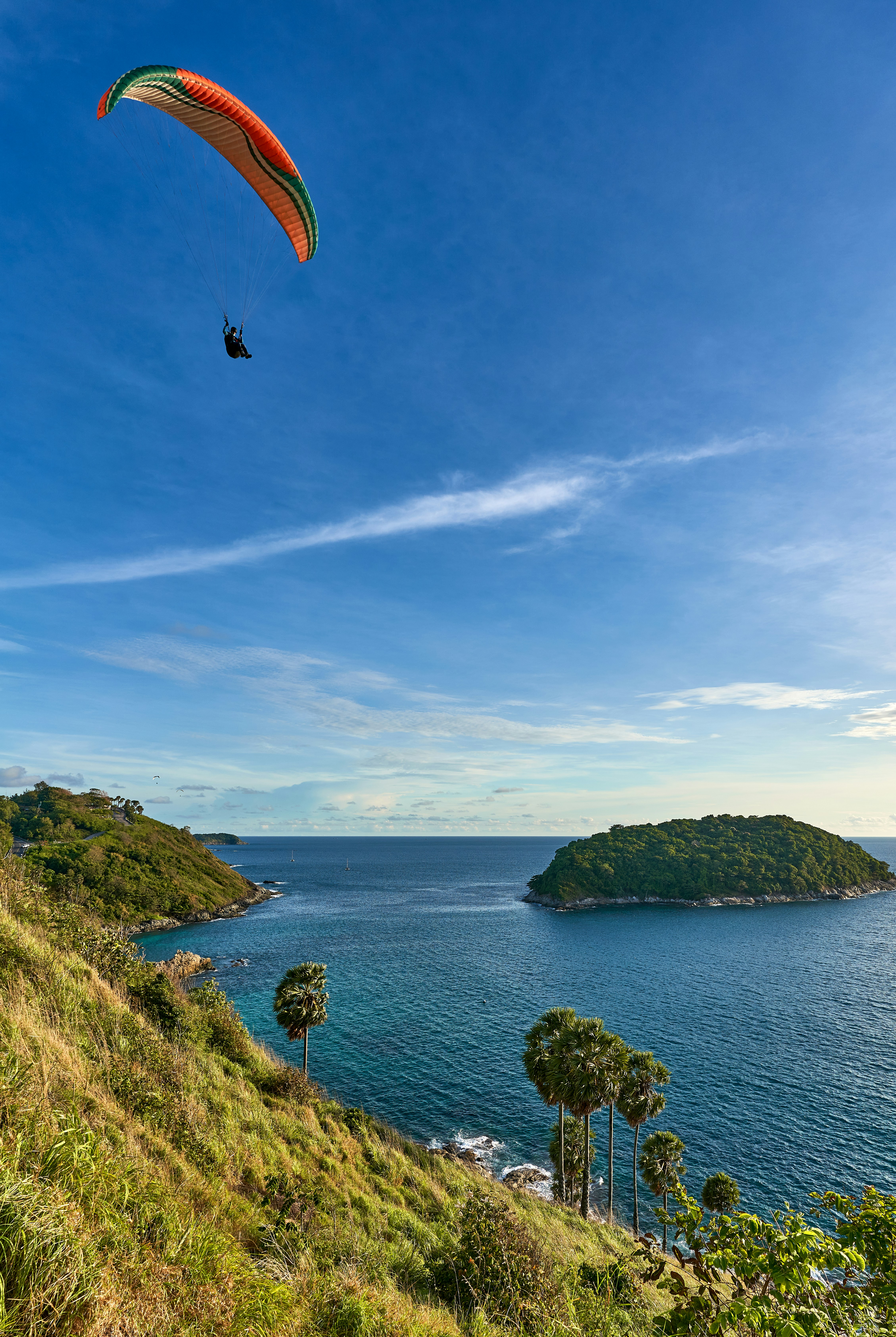 a person paragliding over a lush green hillside next to a body of water