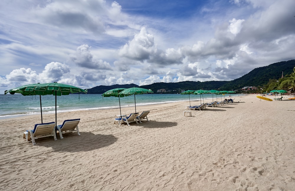 una playa de arena con sillas de jardín y sombrillas