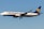 A commercial airplane with the Ryanair logo and branding is flying mid-air against a clear blue sky. It is a Boeing 737, predominantly white with blue and yellow accents.