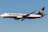 A commercial airplane with the Ryanair logo and branding is flying mid-air against a clear blue sky. It is a Boeing 737, predominantly white with blue and yellow accents.