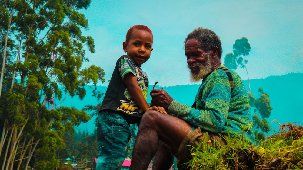 a man sitting next to a child on top of a lush green field