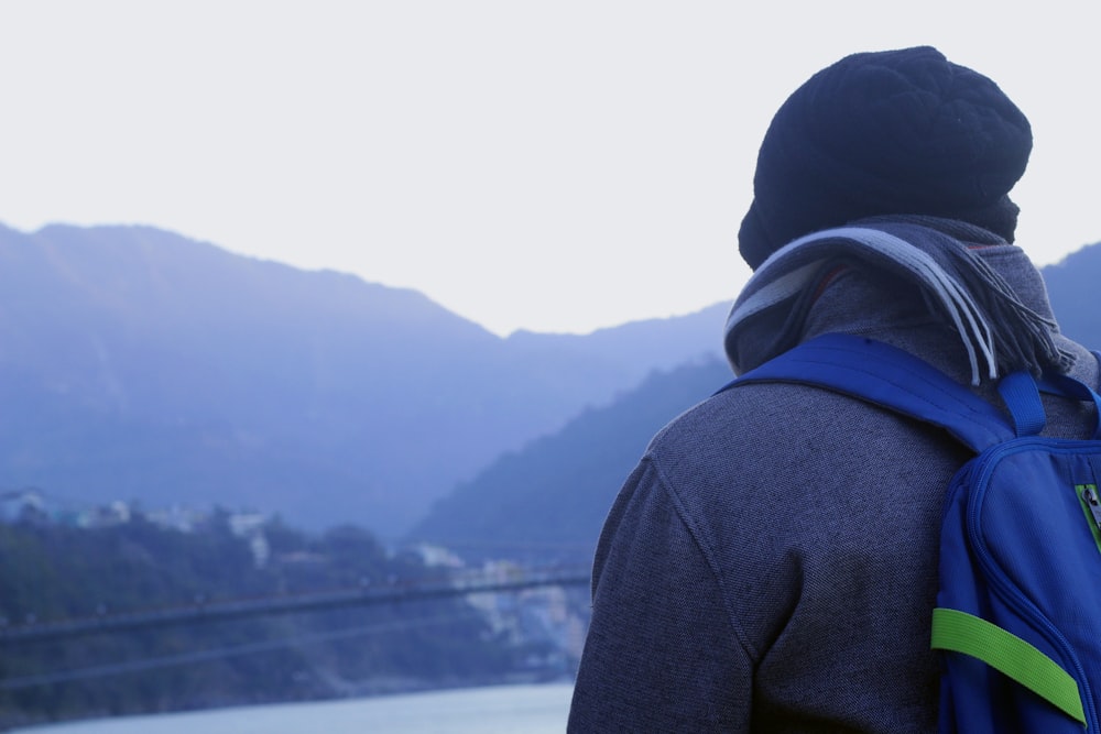 a man with a blue backpack looking out over a body of water