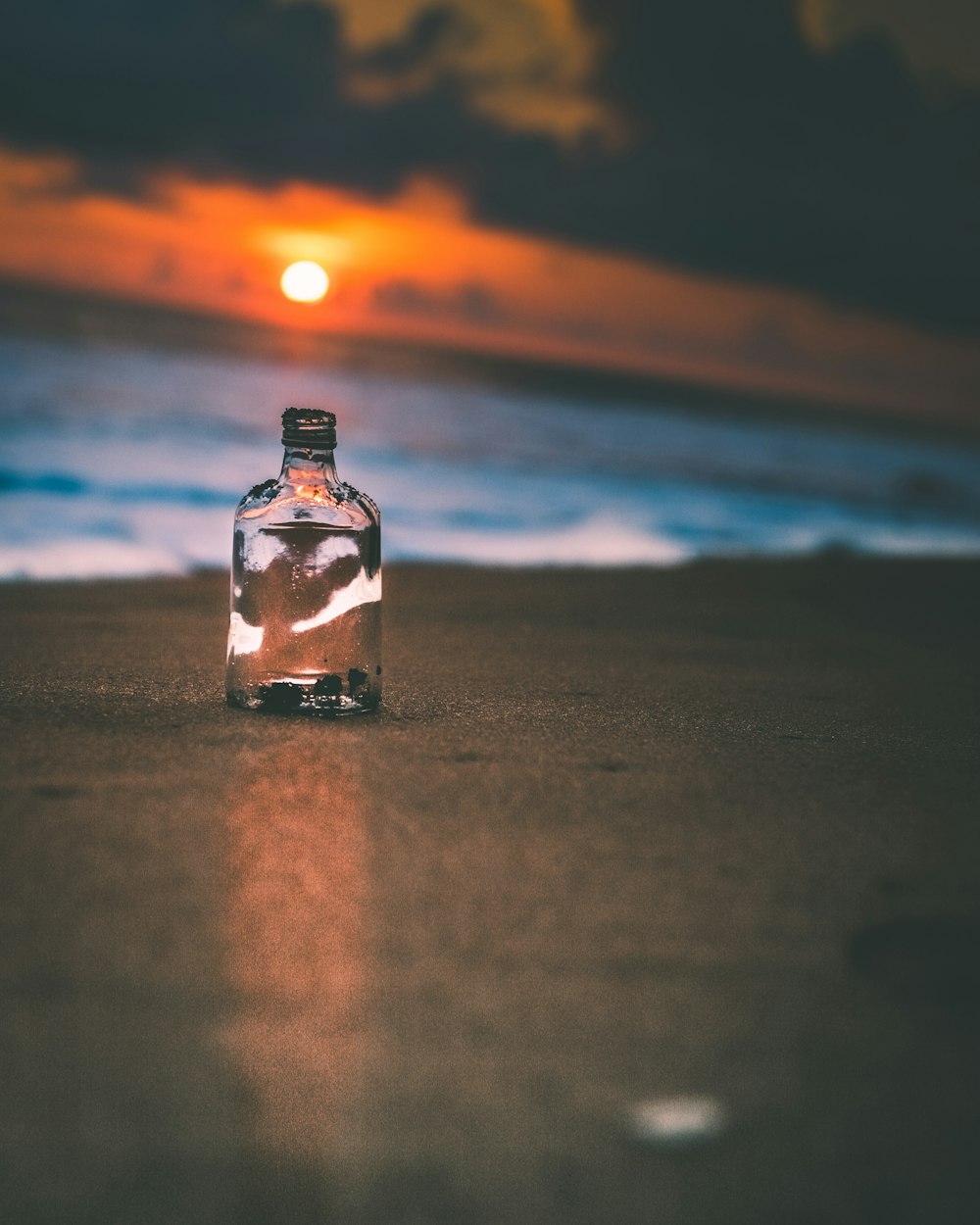 a glass bottle sitting on top of a sandy beach