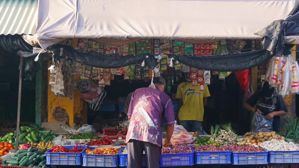 um homem em pé na frente de uma banca de frutas e legumes