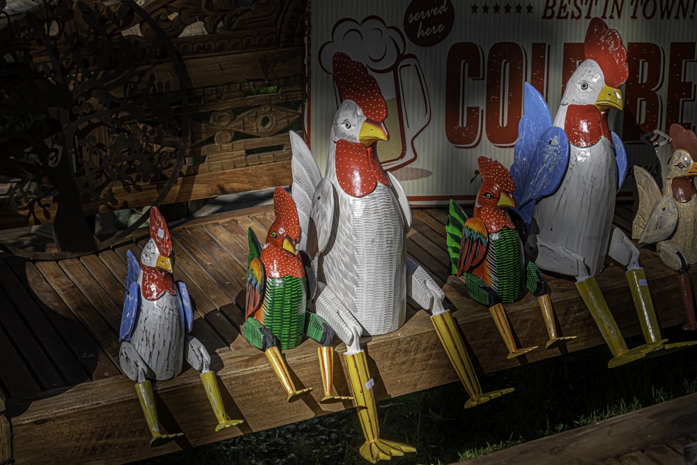 a group of chicken statues sitting on top of a wooden bench