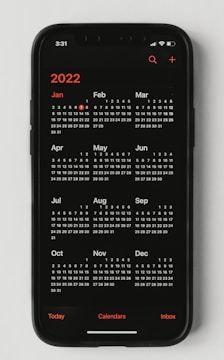 A smartphone displaying a calendar for the year 2022. The months are arranged in three rows on a black screen with white numbers and red accents for the year and certain days.