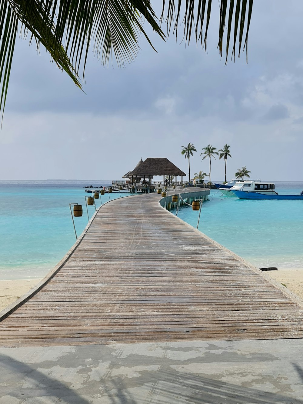 a wooden dock leading to a beach with boats in the water