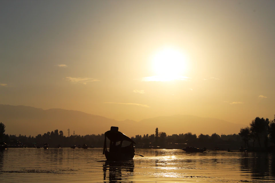 Boat floats on calm waters at sunset behind mountains, surrounded by other boats