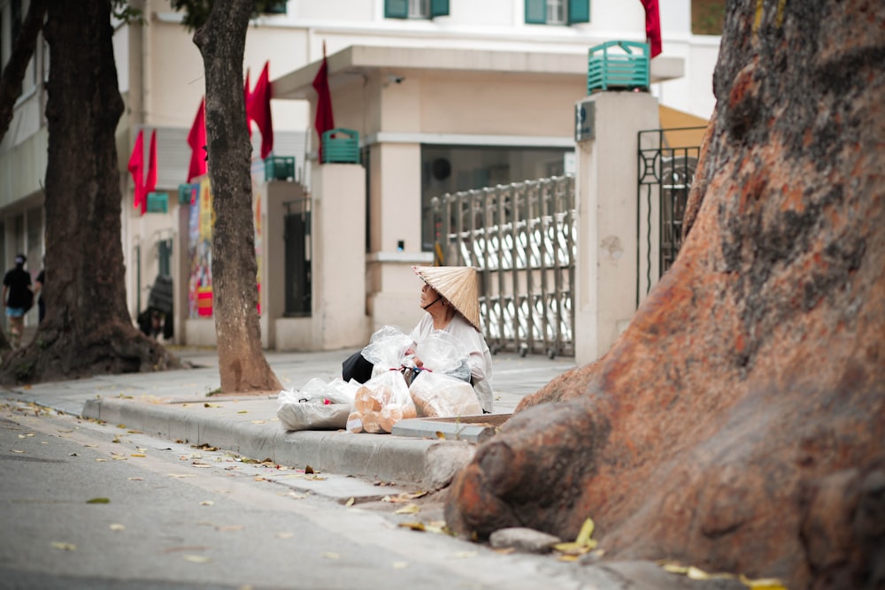 a woman sitting on a curb next to a tree