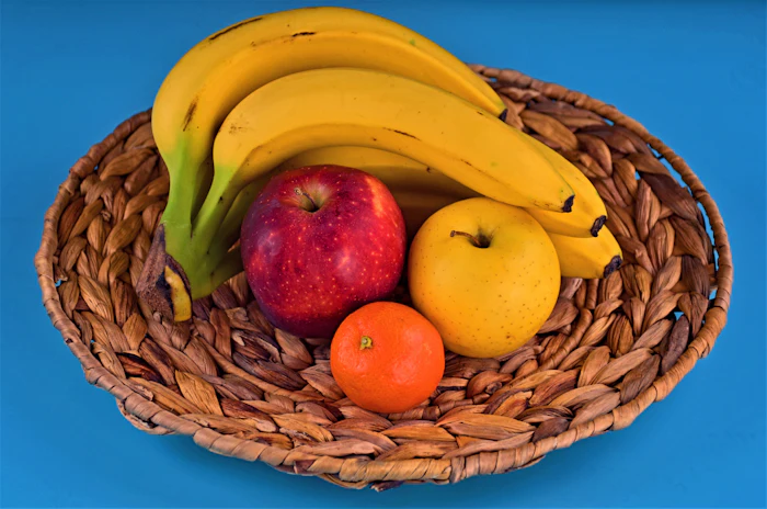 A wicker basket of bananas, apples and oranges