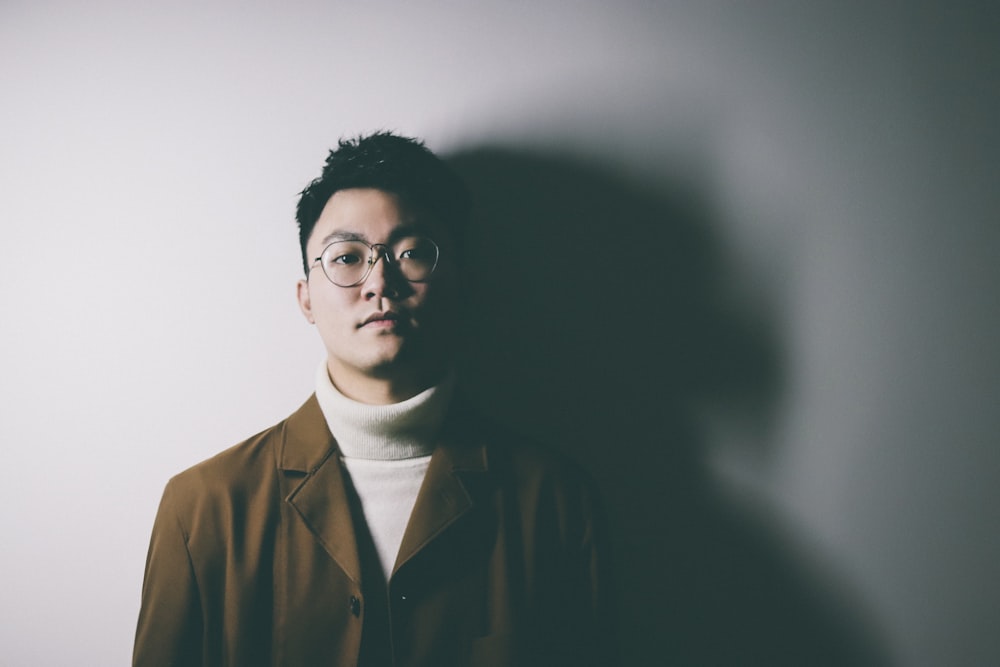 a man wearing glasses standing in front of a white wall