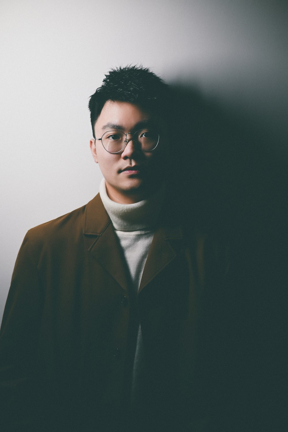 a man wearing glasses standing in front of a white wall