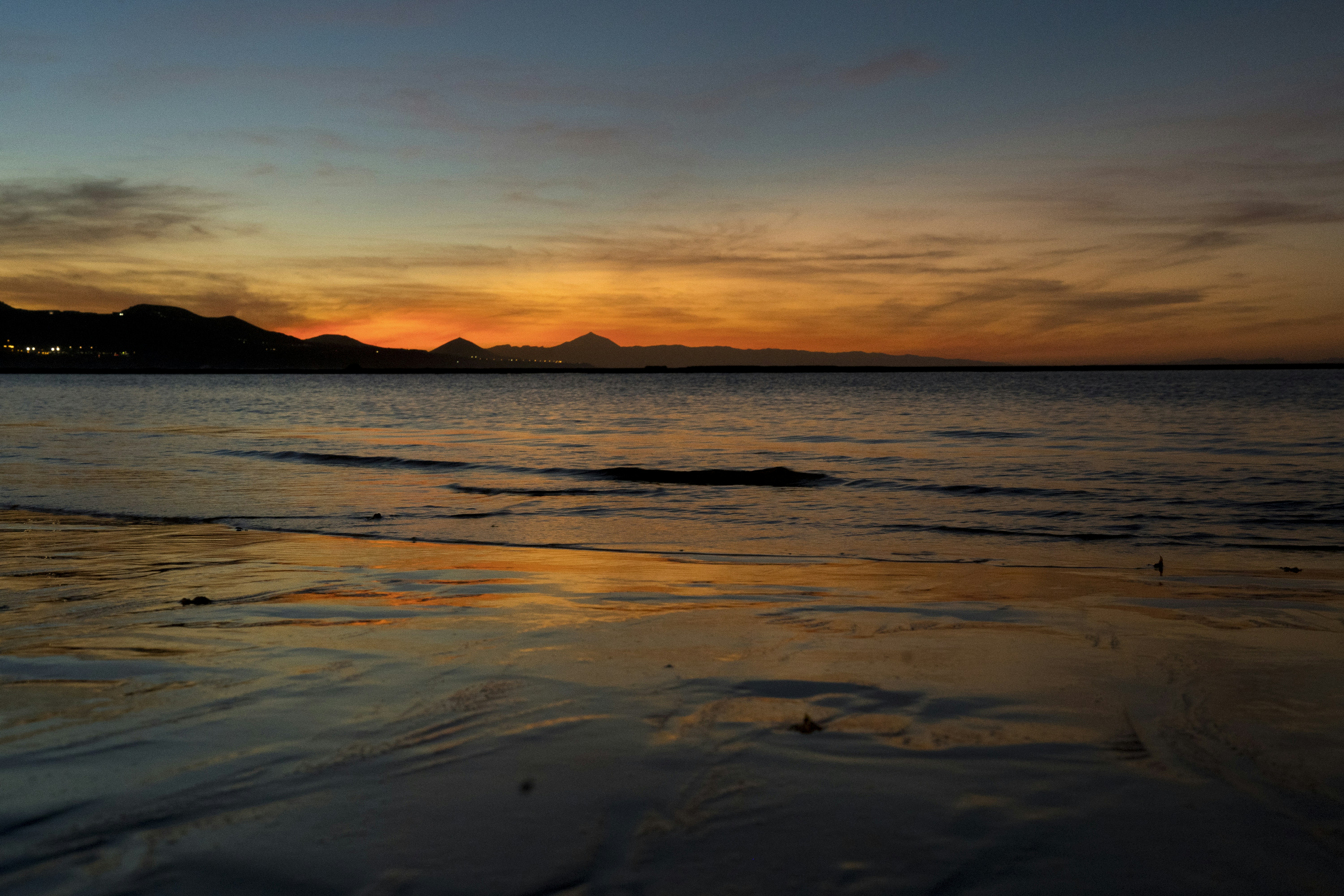 a sunset over a body of water with mountains in the background