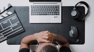 A drama student working on a laptop surrounded by movie scripts and AI design sketches.