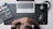 An overhead view featuring a person sitting at a desk with their hands clasped together, looking at a laptop on a dark mouse pad. To the left, there is a film clapperboard, and to the right, a pair of headphones and a computer mouse. The workspace is organized with tech and film elements.