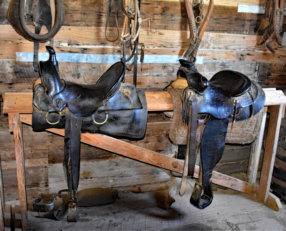 a couple of horse saddles sitting on top of a wooden bench
