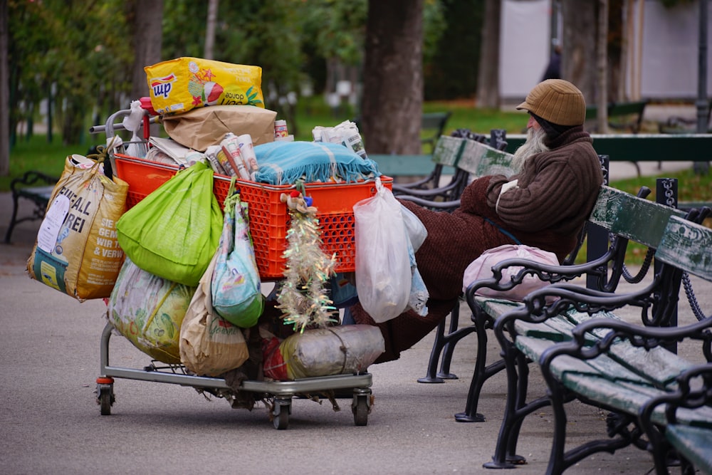 a person sitting on a bench with a cart full of bags