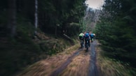 Group of athletes running along a narrow trail through dense forest.