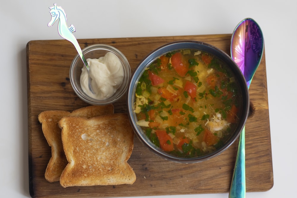 a bowl of soup and a spoon on a cutting board