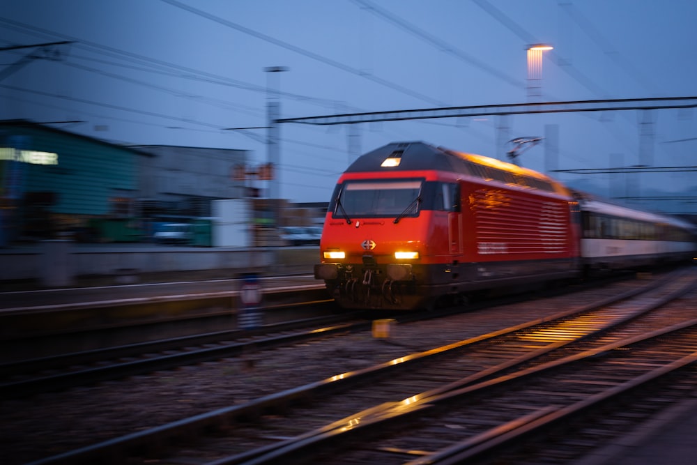 Un treno rosso che viaggia lungo i binari del treno vicino a un edificio