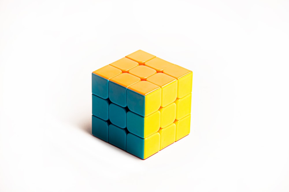 Un cubo amarillo y azul sentado encima de una superficie blanca