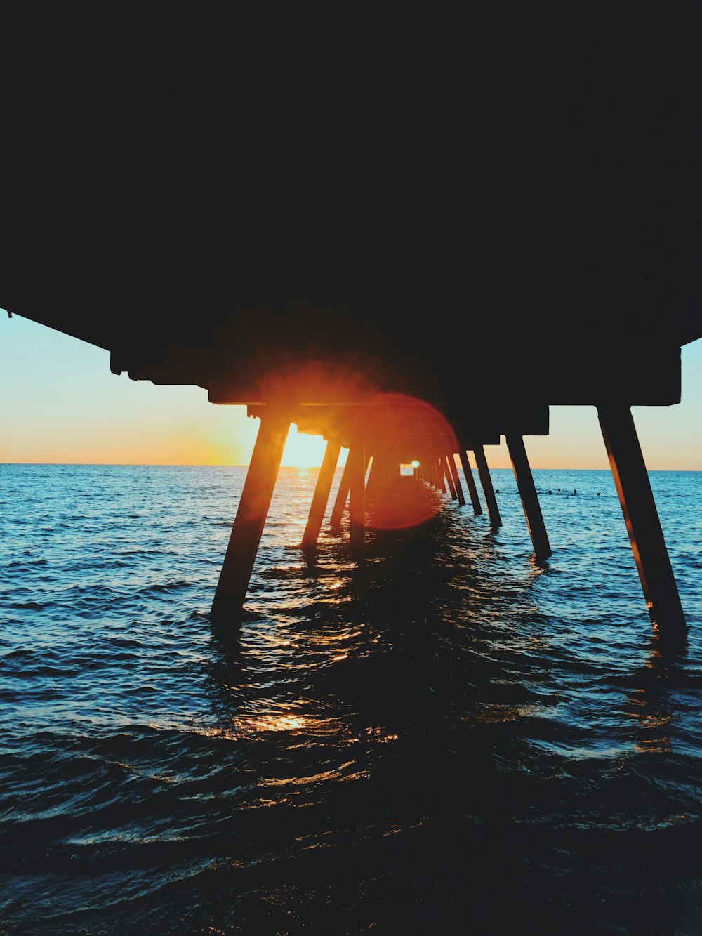 the sun is setting at the end of a pier